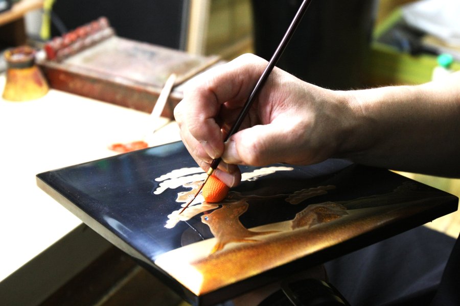 様々な工程を経て行われる蒔絵では、無地の漆が塗られた器に金粉や銀粉、貝などを用いて蒔絵師と呼ばれる職人が装飾を施す繊細な作業。