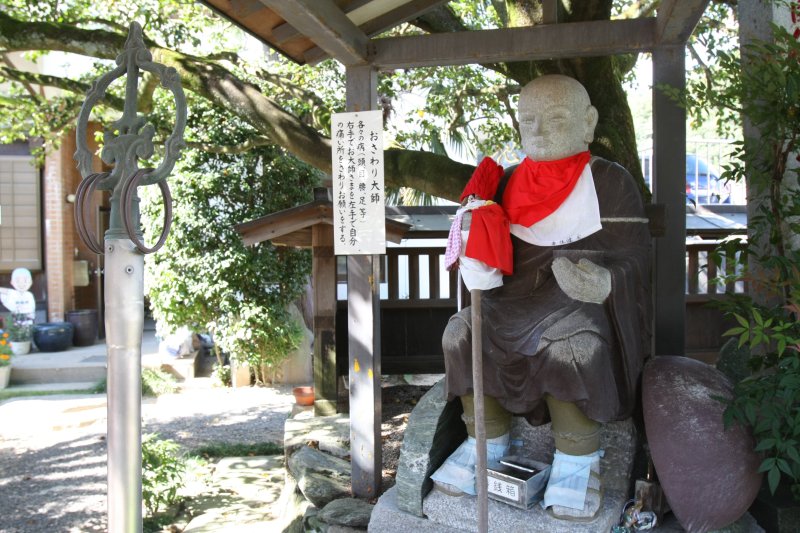 椿の根元にひっそりと佇む優しい表情の「おさわり大師」は、体の悪いところを身代わりになって治してくれると言われている。