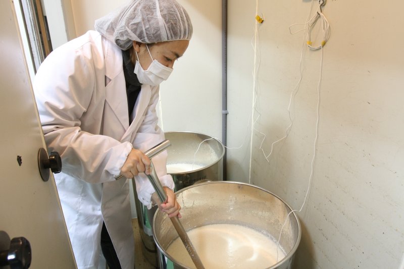 ふつふつと煮えたぎるように発酵する容器の中の酒をかき混ぜ、どぶろくの発酵具合を確認する。